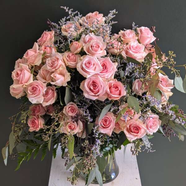 Large arrangement of pink roses with trailing foliage in a clear glass vase