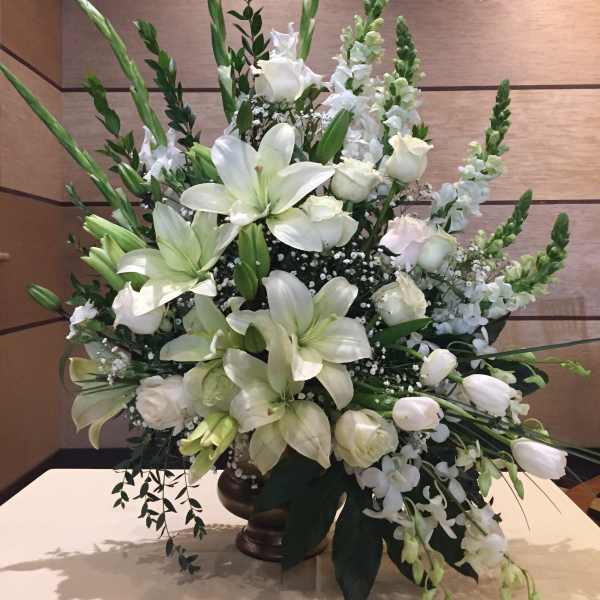White lilies and roses arranged in a tall vase centerpiece