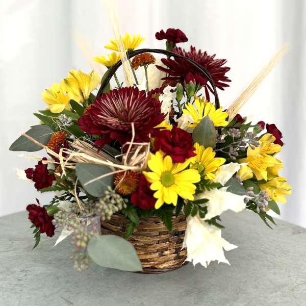 Basket arrangement of yellow and burgundy flowers with dried accents
