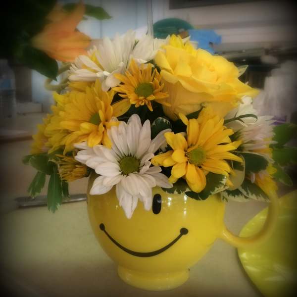Yellow smiley-face mug filled with yellow and white daisies