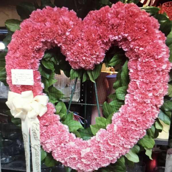 Pink heart-shaped floral wreath on an easel with a white ribbon bow