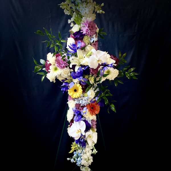 Tall cross-shaped standing spray with white lilies, orchids, mums and colorful daisies on a metal easel