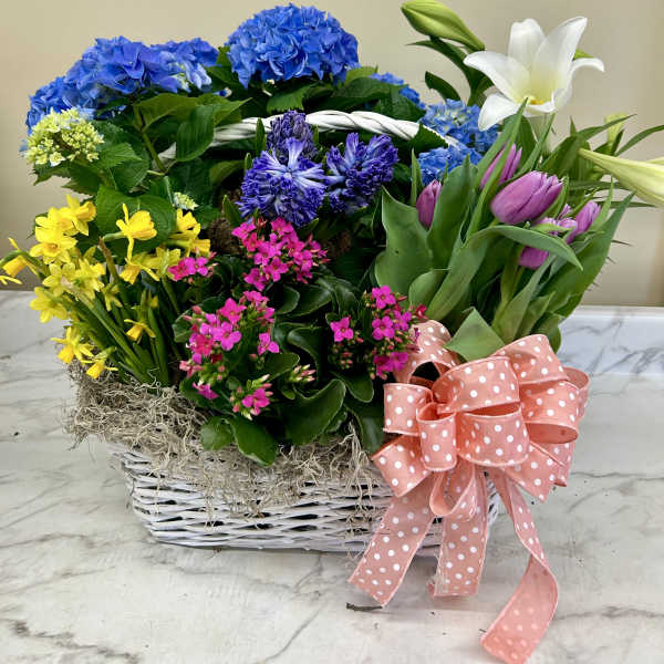 Basket arrangement with blue hydrangeas, yellow daffodils, pink flowers, and white lilies