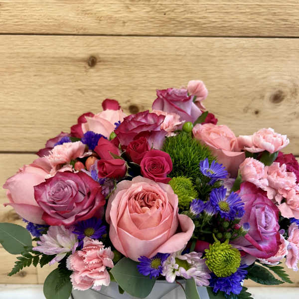 Pink and purple mixed flower arrangement in a round hat box with ribbon