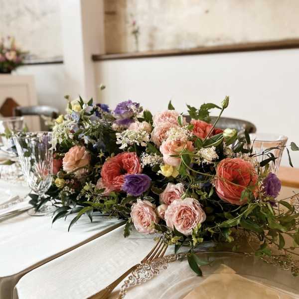 Low floral centerpiece with pink, peach, purple, and white blooms on a table