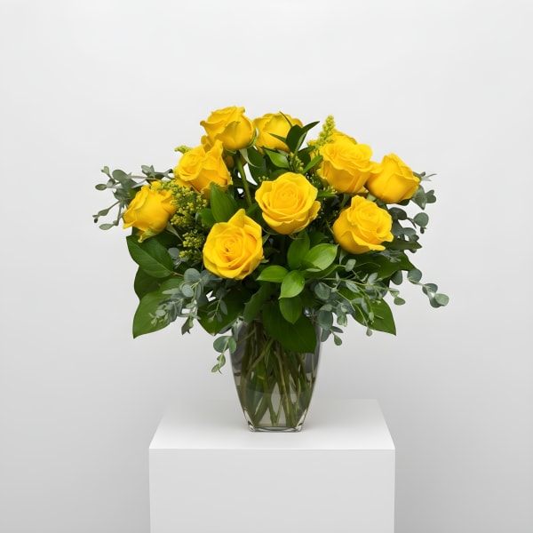 Arrangement of bright yellow roses in a clear glass vase with lush filler accents.