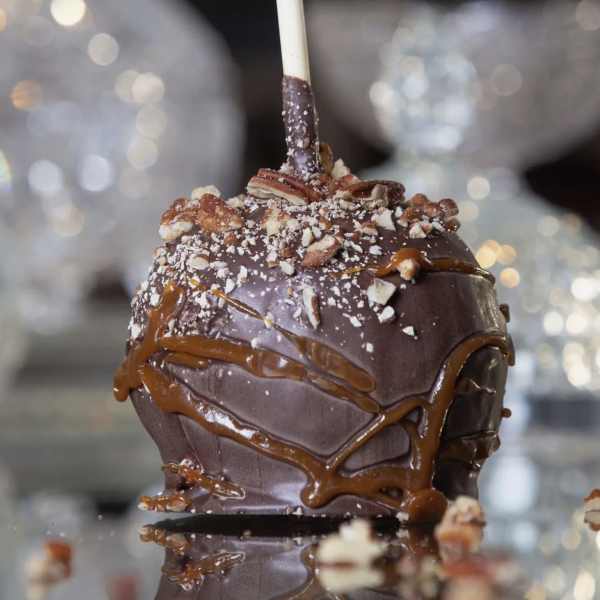 Chocolate dipped caramel apple on a stick, topped with chopped nuts and caramel drizzle
