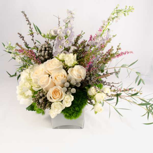 Cream roses and white blossoms in a square glass vase