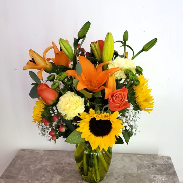 Mixed bouquet with orange lilies, sunflowers, and roses in a glass vase