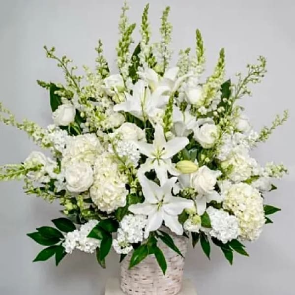 White floral arrangement in a woven basket with lilies and roses