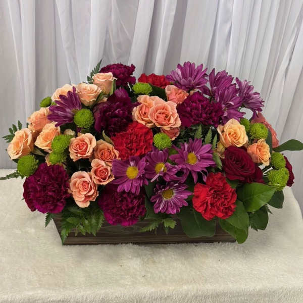 Mixed bouquet of roses, carnations, and purple daisies in a rectangular container