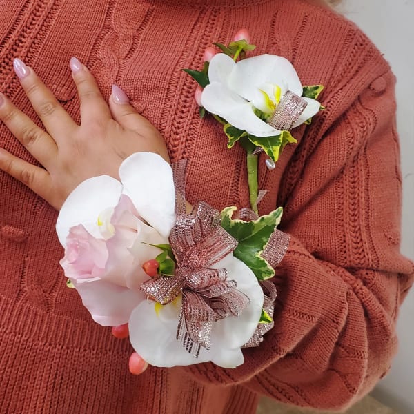 White orchid corsage with pink ribbon accents worn on a sweater