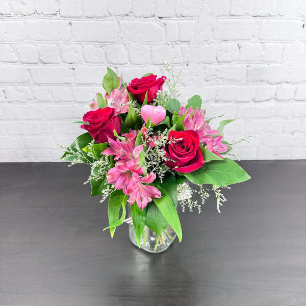 Pink roses and alstroemeria in a clear glass vase with a pink heart pick