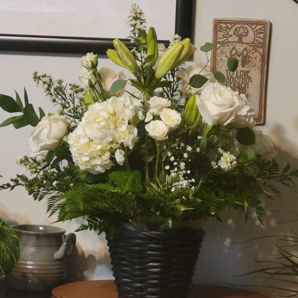 White roses and lilies arranged in a black basket vase