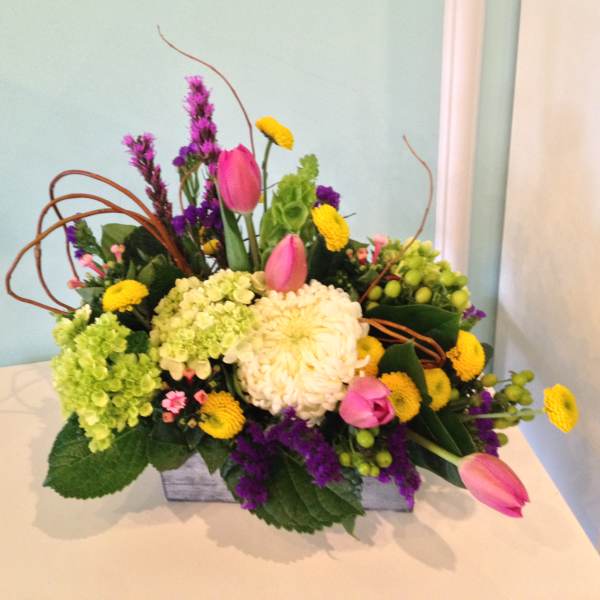Mixed bouquet with pink tulips, hydrangeas, and yellow blooms in a low container