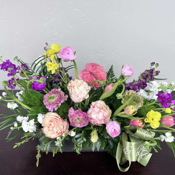 Low floral arrangement with pink, purple, yellow, and white blooms in a rectangular container