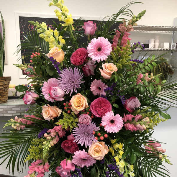 Tall standing spray of pink, peach, lavender, and yellow flowers on a metal easel.