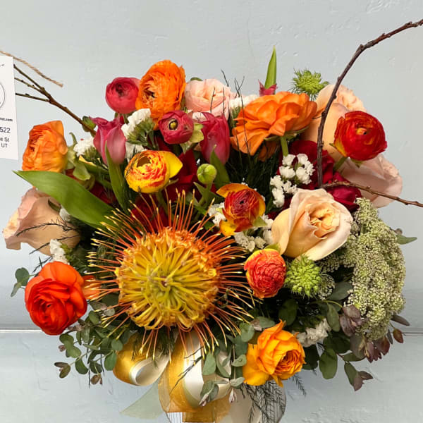 Bright mixed bouquet with orange, red, and peach flowers in a glass vase