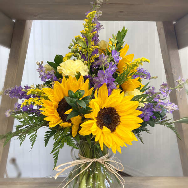Bouquet of sunflowers, purple flowers, and yellow blooms in a glass vase