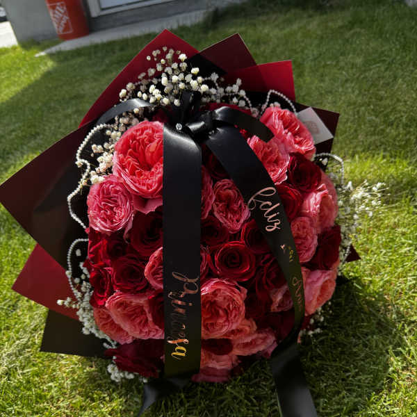 Bouquet of red and pink roses with black ribbon and white filler flowers