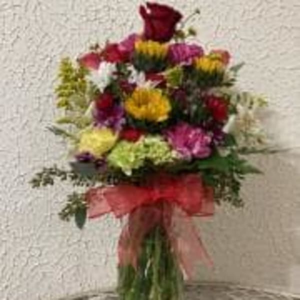 Tall mixed bouquet in a glass vase with a pink ribbon