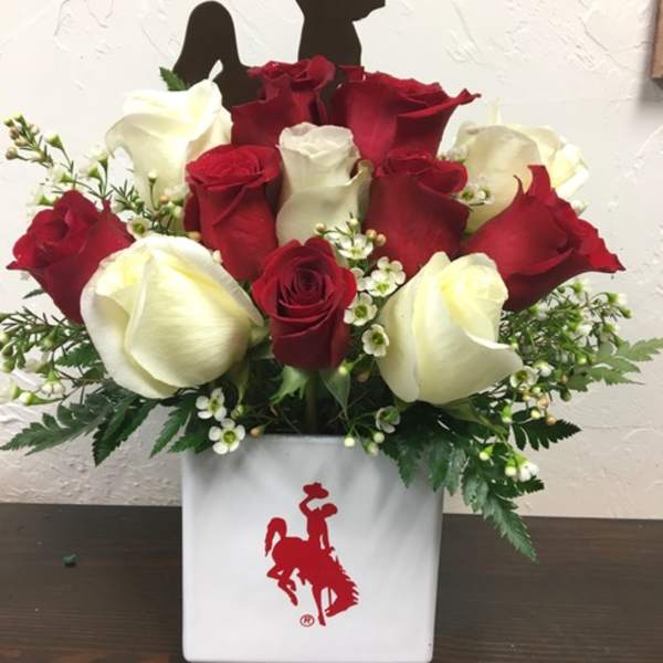 Red and white roses arranged in a white vase with a cowboy silhouette topper
