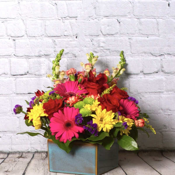 Bright mixed flower arrangement in a square blue vase
