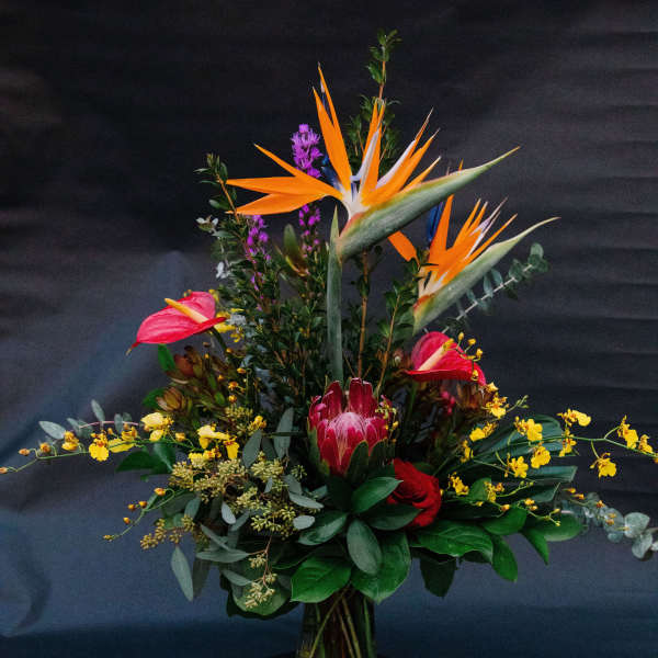 Tropical bouquet with orange bird-of-paradise and pink anthuriums in a glass vase
