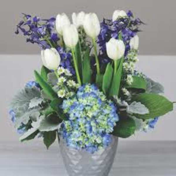 White tulips and blue flowers in a silver vase