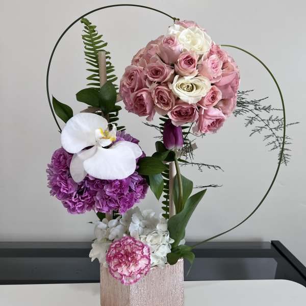 Pink and white floral arrangement in a rose-gold box with circular wire accents.