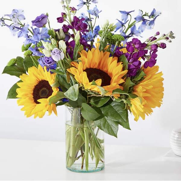 Bouquet of sunflowers, purple blooms, and blue flowers in a glass vase
