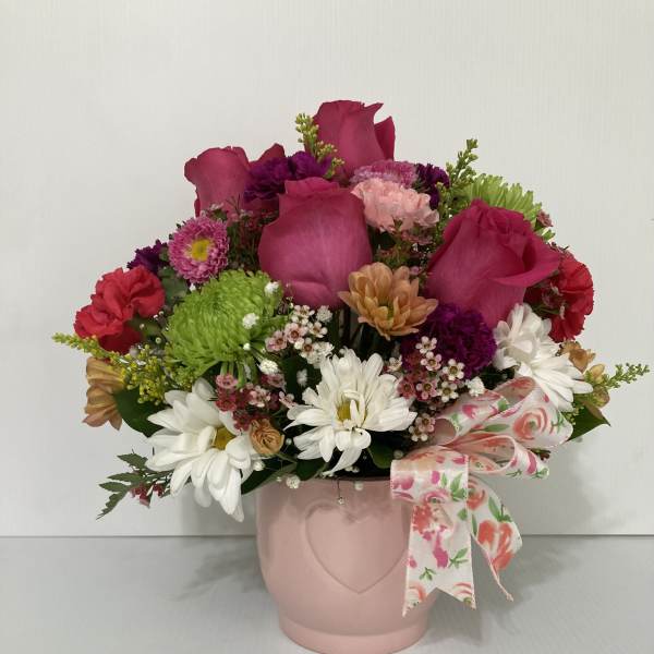 Mixed pink and white flowers in a pink vase with a floral ribbon