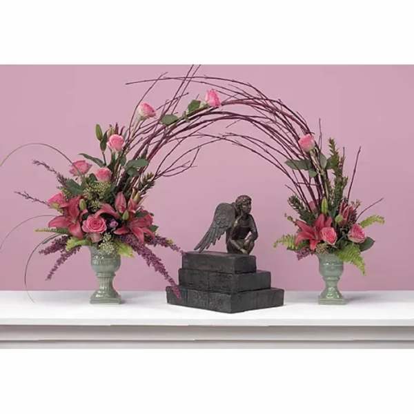 Two pink floral arrangements flank a dark angel statue on stacked blocks