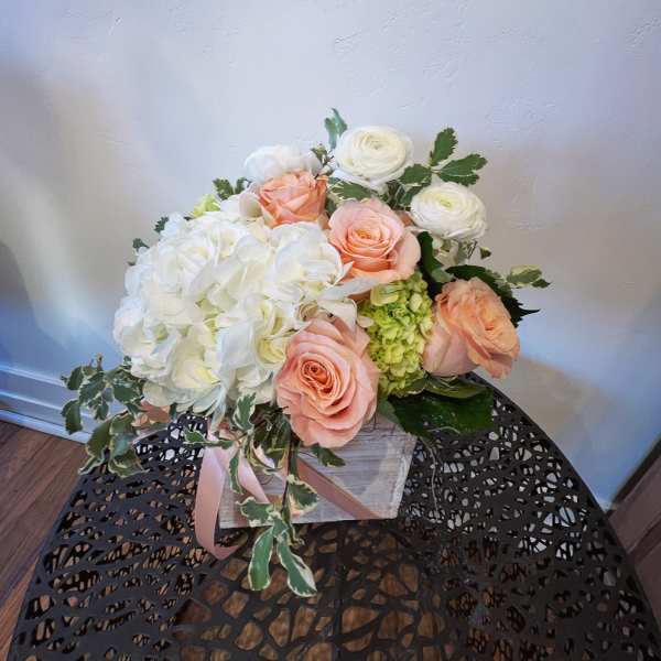 Low arrangement of white hydrangeas, peach roses, and white blooms in a rustic wooden box.