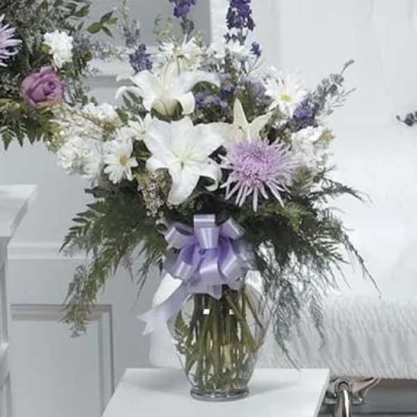 White and lavender floral arrangement in a glass vase with a ribbon
