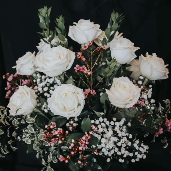 White roses arranged with pink berries and baby's breath