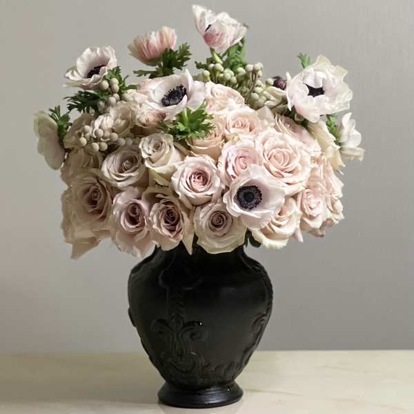 Blush roses and pale anemones arranged in a black vase