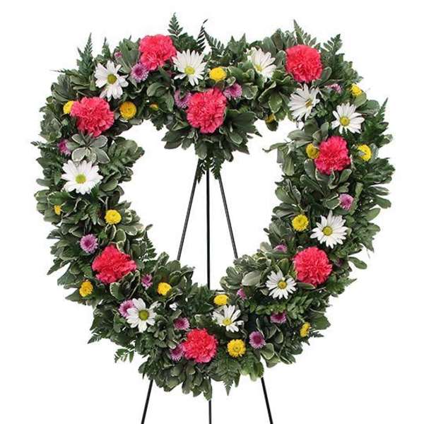 Heart-shaped floral wreath on a stand with pink, white, and yellow flowers