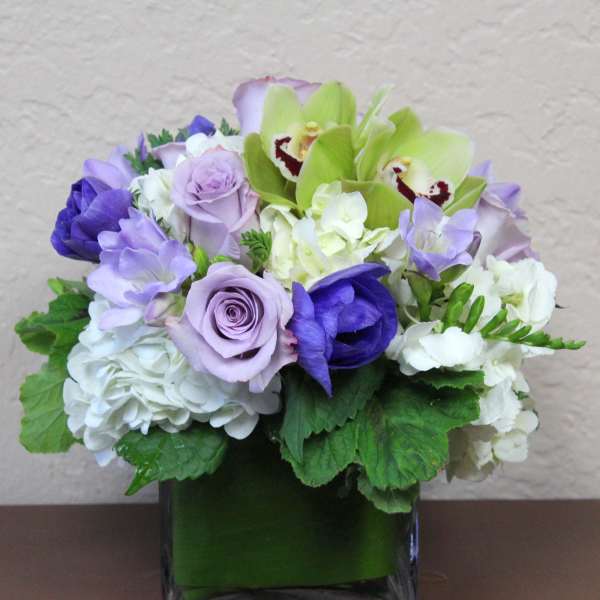 Lavender and white floral arrangement in a square glass vase