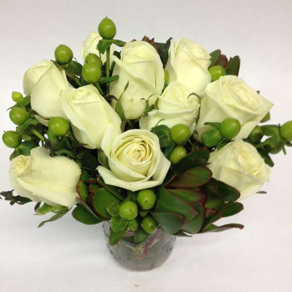 White rose bouquet in a glass vase with green berries