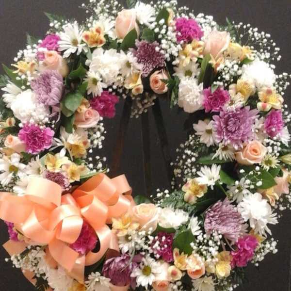 Circular floral wreath with pink, white, and peach flowers on a black stand
