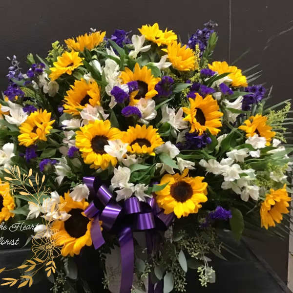 Large bouquet of sunflowers, white flowers, and purple blooms with a ribbon