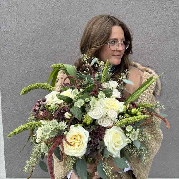 Woman holding a large bouquet of white and pale yellow roses with green accents