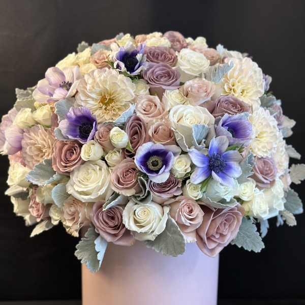 Round bouquet of pastel roses and purple flowers in a pink box
