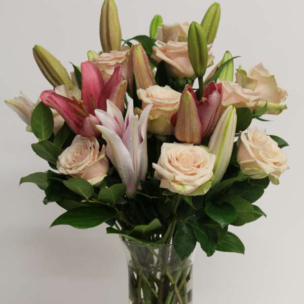 Tall vase of blush roses and pink lilies arranged in a clear glass cylinder