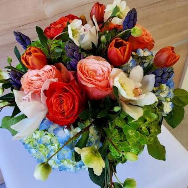 Compact arrangement of orange tulips, mixed roses, orchids, and blue and green hydrangeas.