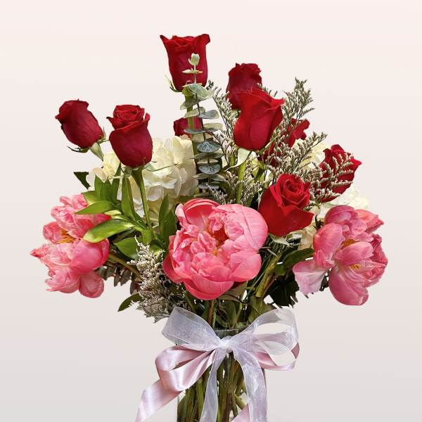 Bouquet of red roses and pink peonies in a glass vase with a ribbon