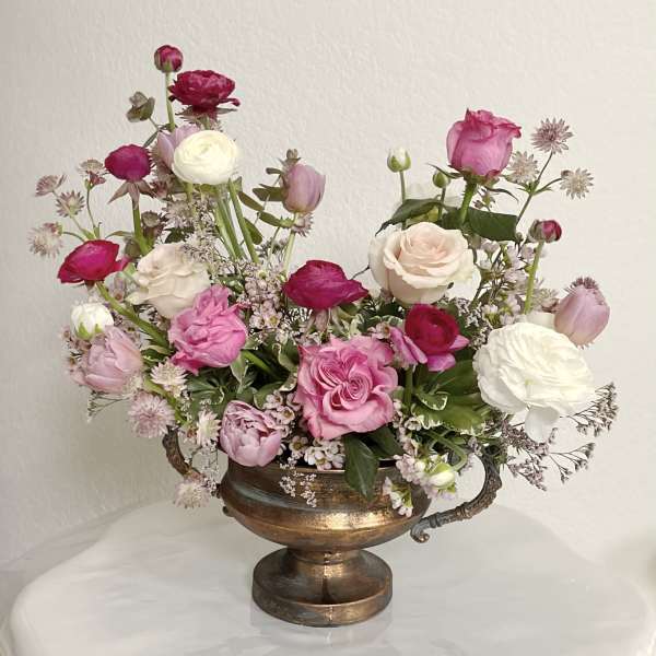 Pink and white mixed flowers arranged in a bronze urn vase