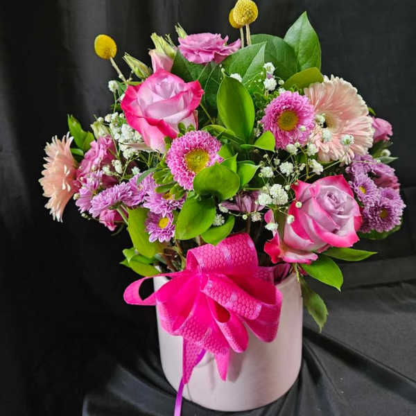 Pink roses, gerberas, and mums arranged in a pale pink hatbox with a bright pink bow