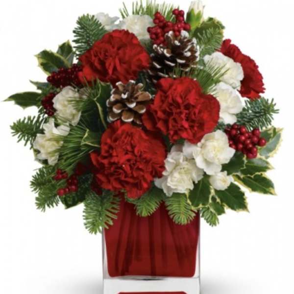 Red and white floral arrangement in a clear vase with pinecones and berries